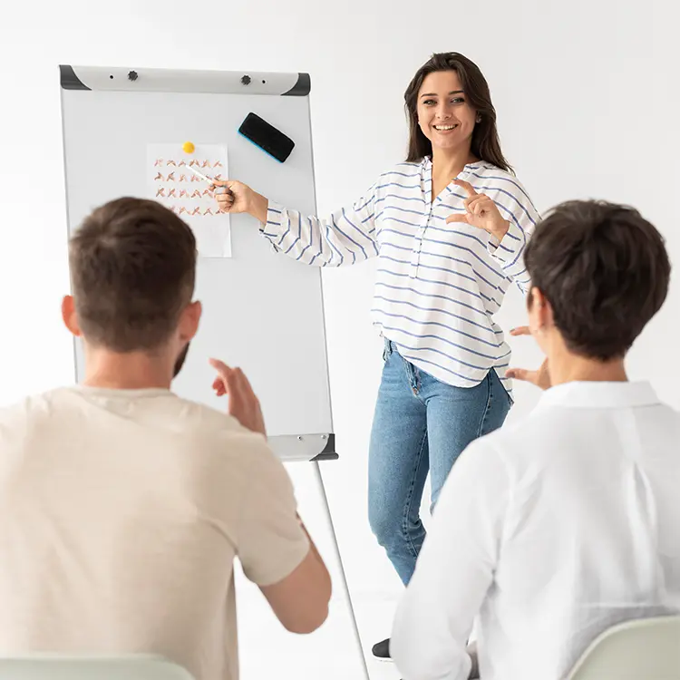 Female instructor pointing to a chart and demonstrating sign language hand gestures to students during a classroom lesson
