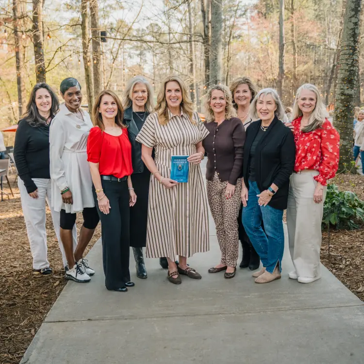 Group portrait of professional women attending an outdoor book signing and networking event in a park setting.
